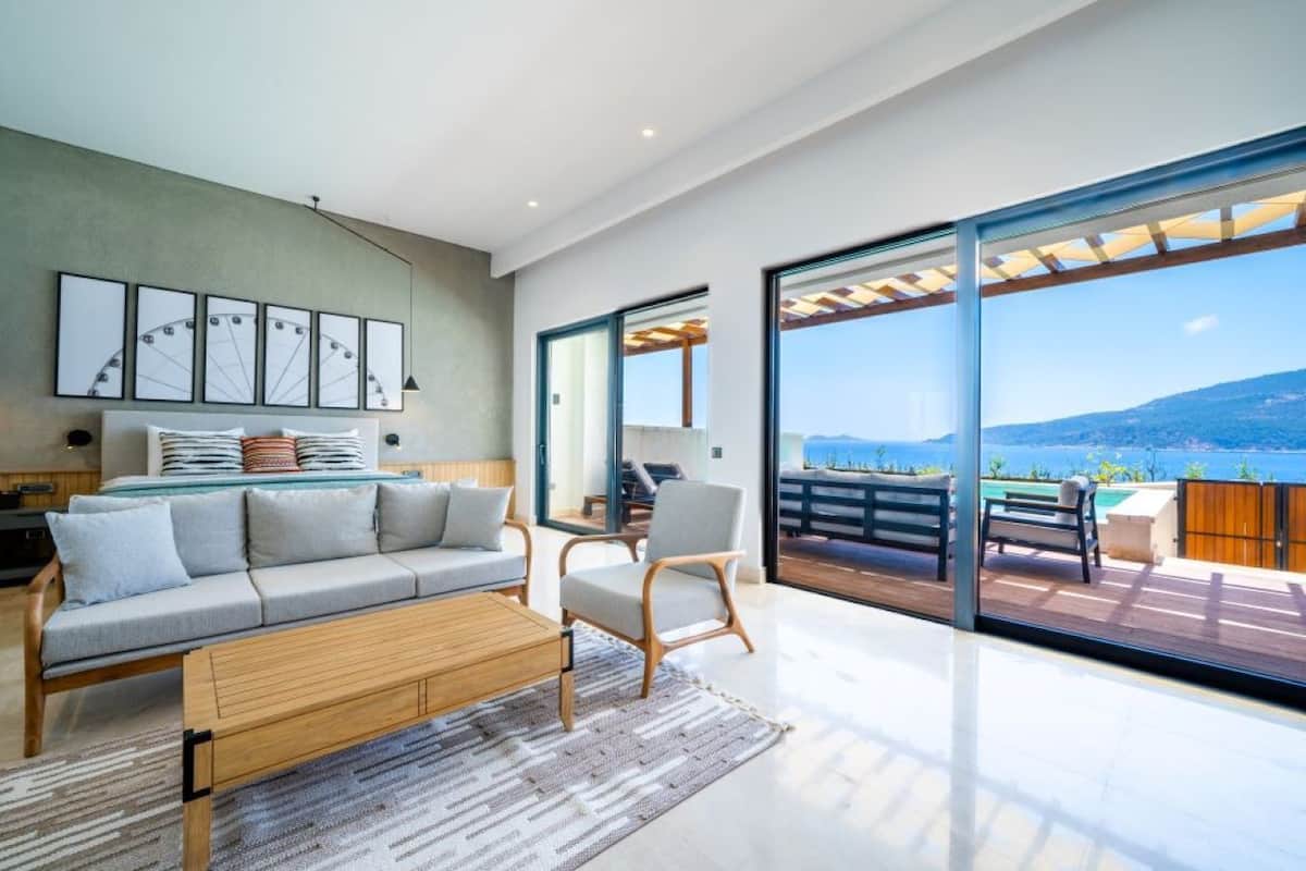 Un salón moderno con sofá, sillón y vista al mar a través de amplios ventanales correderas.