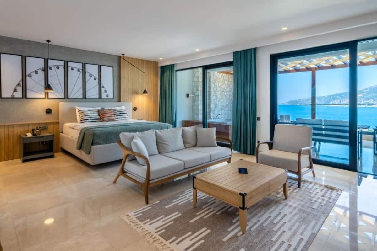 Habitación de hotel moderna con cama, sofá, sillón y una mesa de centro. Amplia ventana con vistas al mar.