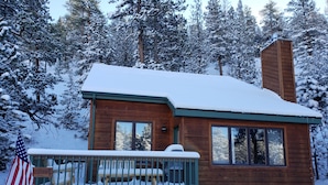 Eine Holzhütte mit einer verschneiten Veranda und einem Schornstein.