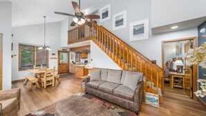 Ein geräumiges Wohnzimmer mit Holztreppe, einer Couch, einem Esstisch und einem Deckenventilator.