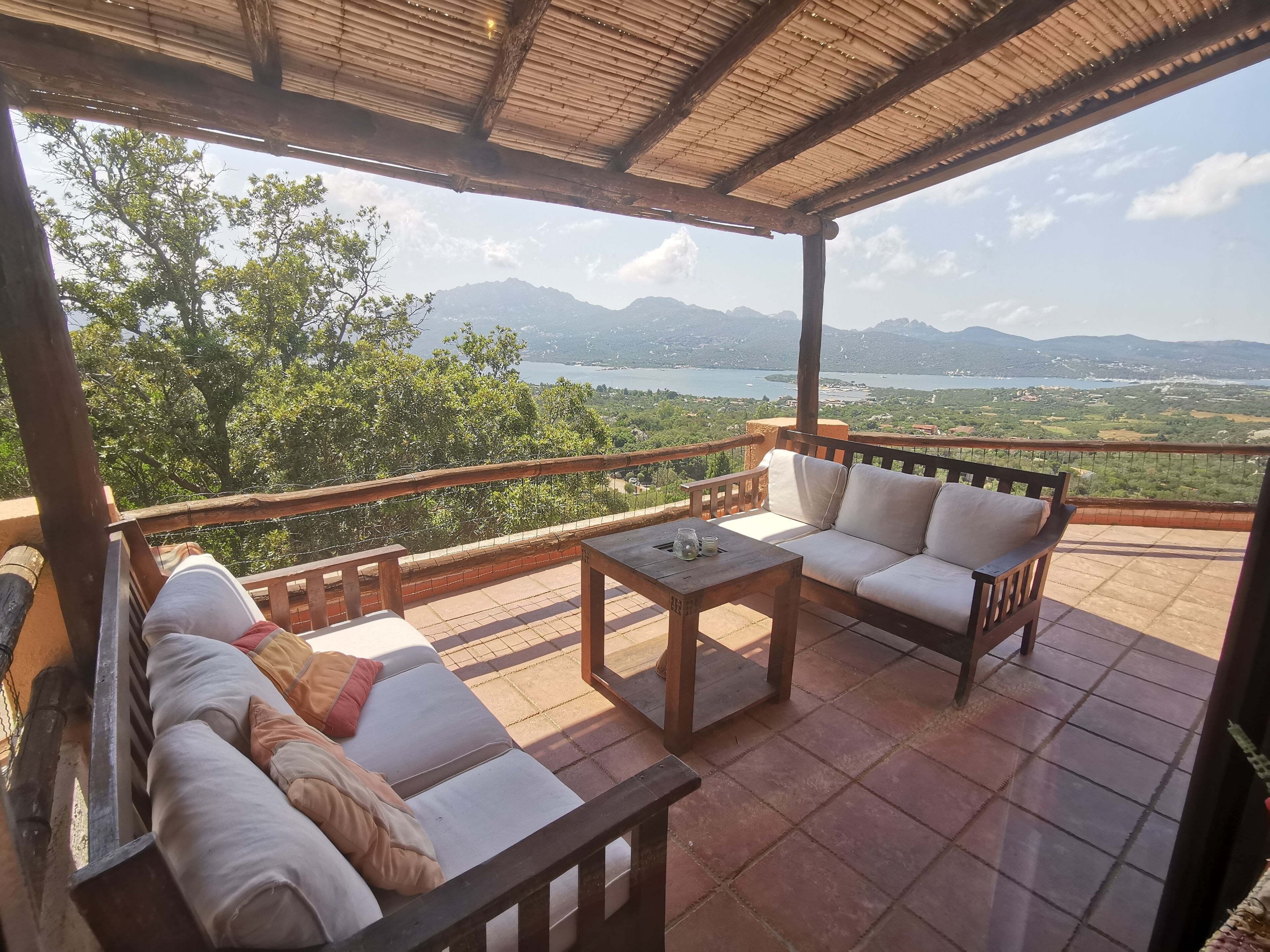 Un espace extérieur aménagé, abrité et doté d’un canapé et d’une table, offrant une vue panoramique sur un paysage magnifique, avec des montagnes et un lac.