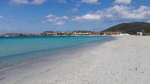 A beach with clear turquoise water, white sand, and a backdrop of buildings and hills. - Villa Vista, from the terrace a stunning view to  Costa Smeralda and the Islands (Sardegna)