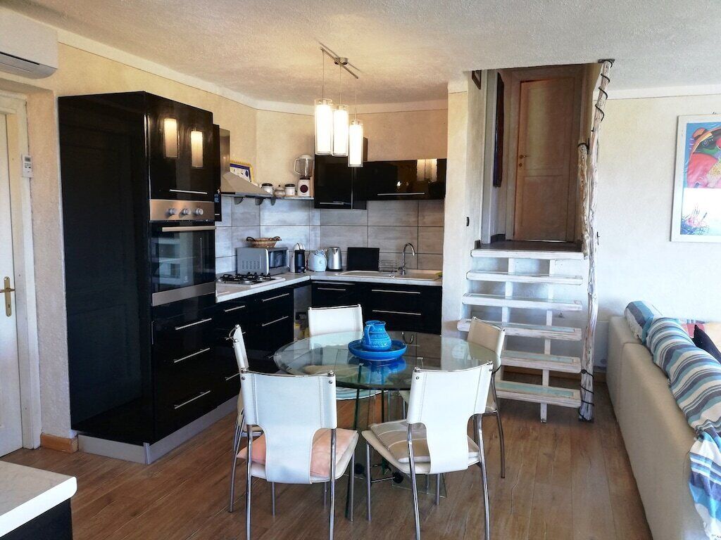 A compact kitchen with black cabinets, a glass dining table, and white chairs.