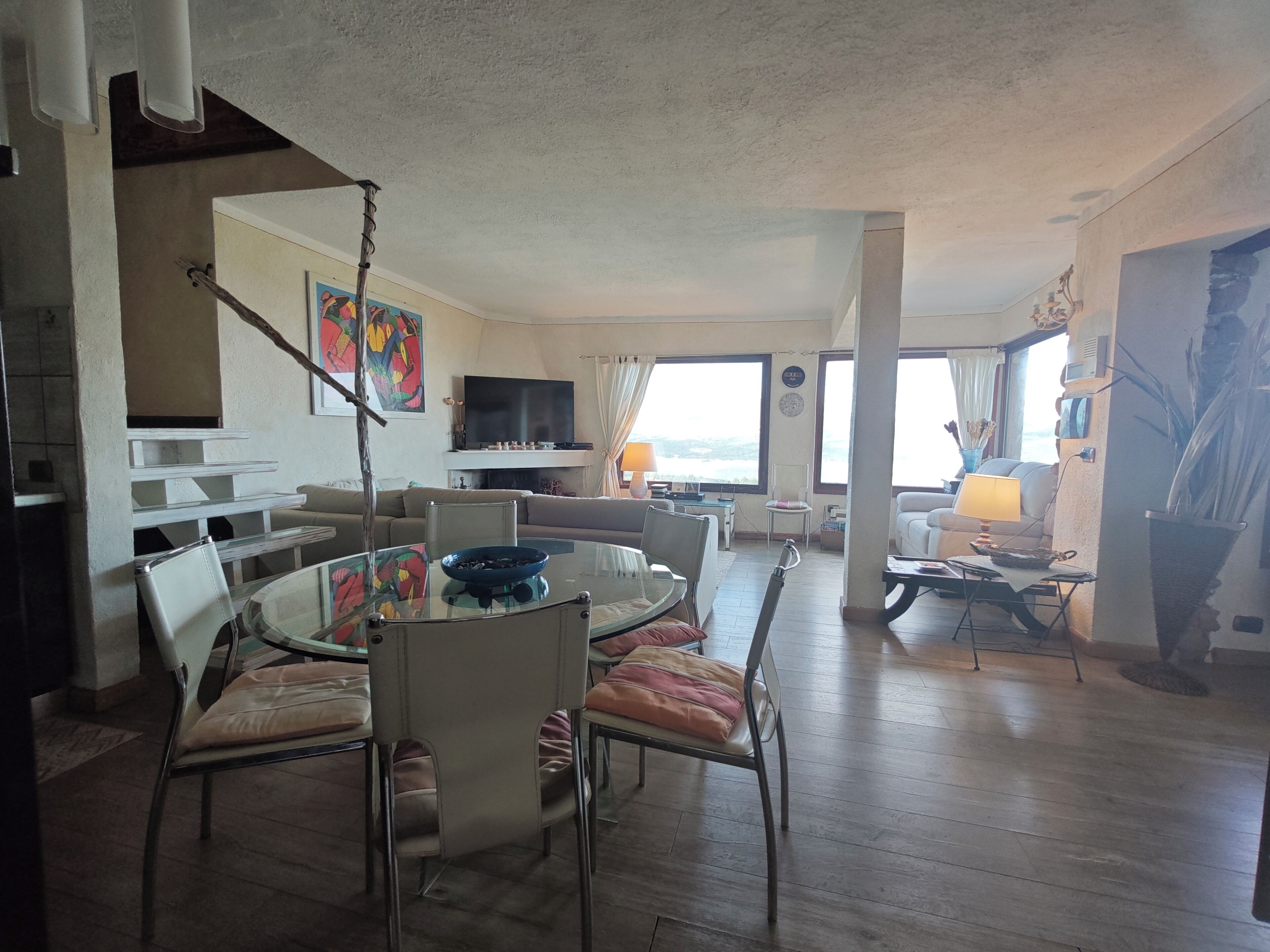 A spacious living room with a round dining table, comfortable seating, a flat-screen TV, and a large window offering a view.