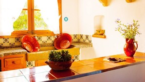 A kitchen with a window, a sink, a bowl of plants, and a red vase.