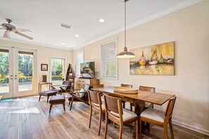 Un coin repas avec une table et des chaises en bois, un ventilateur de plafond et un tableau accroché au mur.
