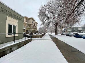 A snow-covered sidewalk adjacent to a building with a stone wall and a metal railing.
