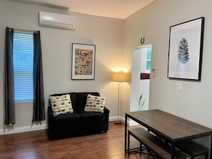 A living room with a black sofa, a wooden table, a floor lamp, and framed pictures on the walls.