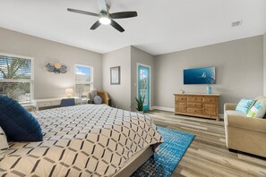 Un dormitorio con cama, ventilador de techo, televisor, cómoda y ventana con persianas.
