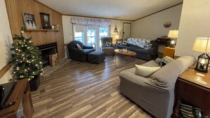 Ein Wohnzimmer mit Kamin, Weihnachtsbaum, Sofa, Sessel und Couchtisch.