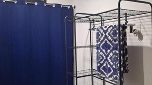 Een badkamer met douchegordijn, een metalen droogrek en een airconditioning.