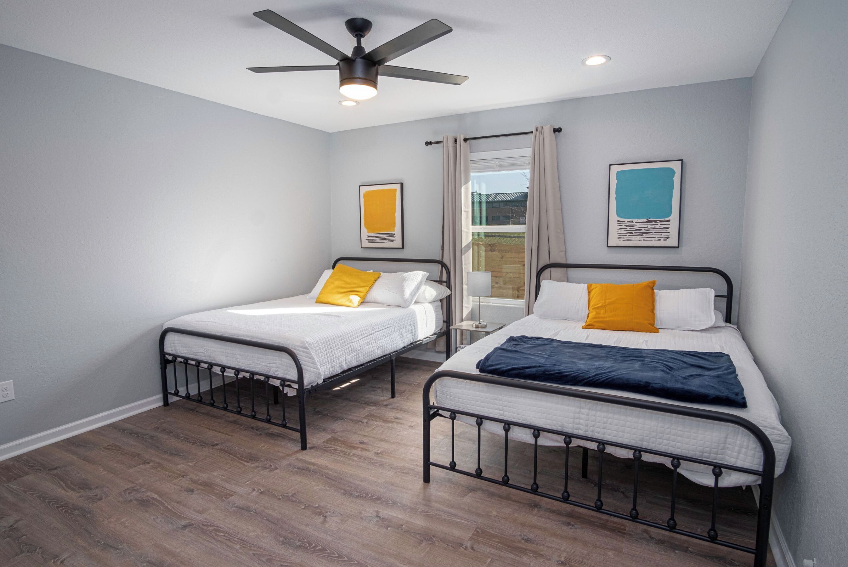 A bedroom with two single beds, a ceiling fan, and a window with curtains.