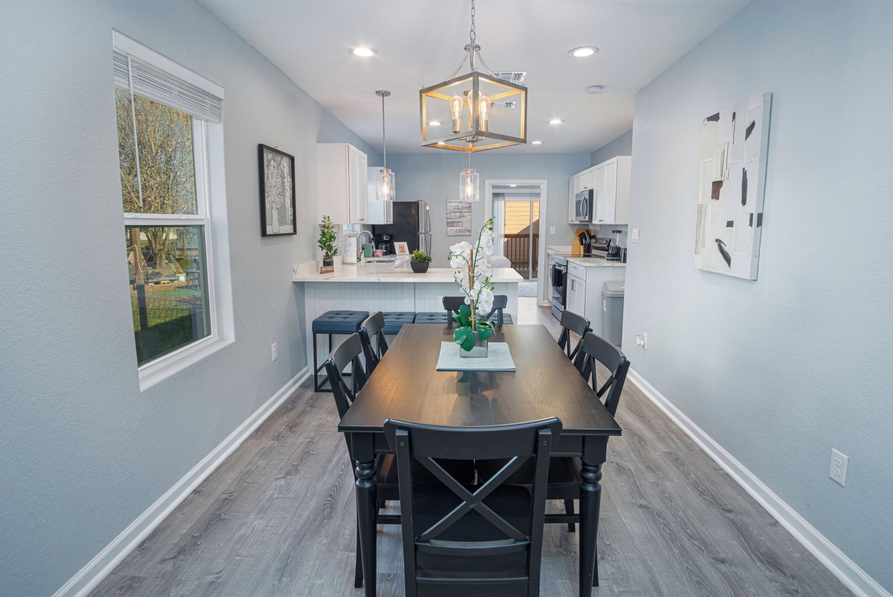 A modern kitchen with white cabinets, a wooden dining table, and a chandelier.
