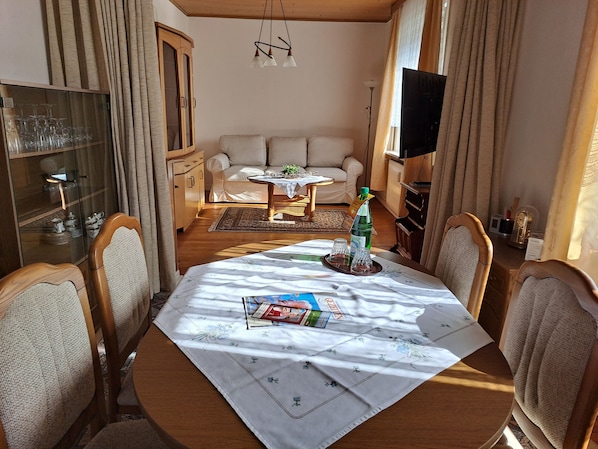 A dining area with a wooden table, chairs, a sofa, and a television. - Relax in the iodine-rich North Sea air in the first floor apartment Deichblick (Friedrichskoog)