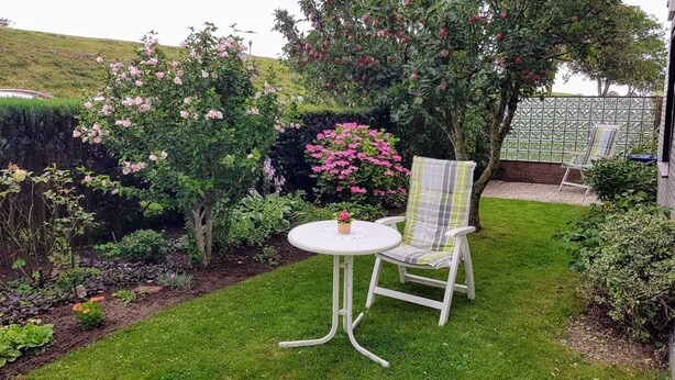 En trädgård med ett vitt bord och en stol, omgiven av olika växter och blommor.