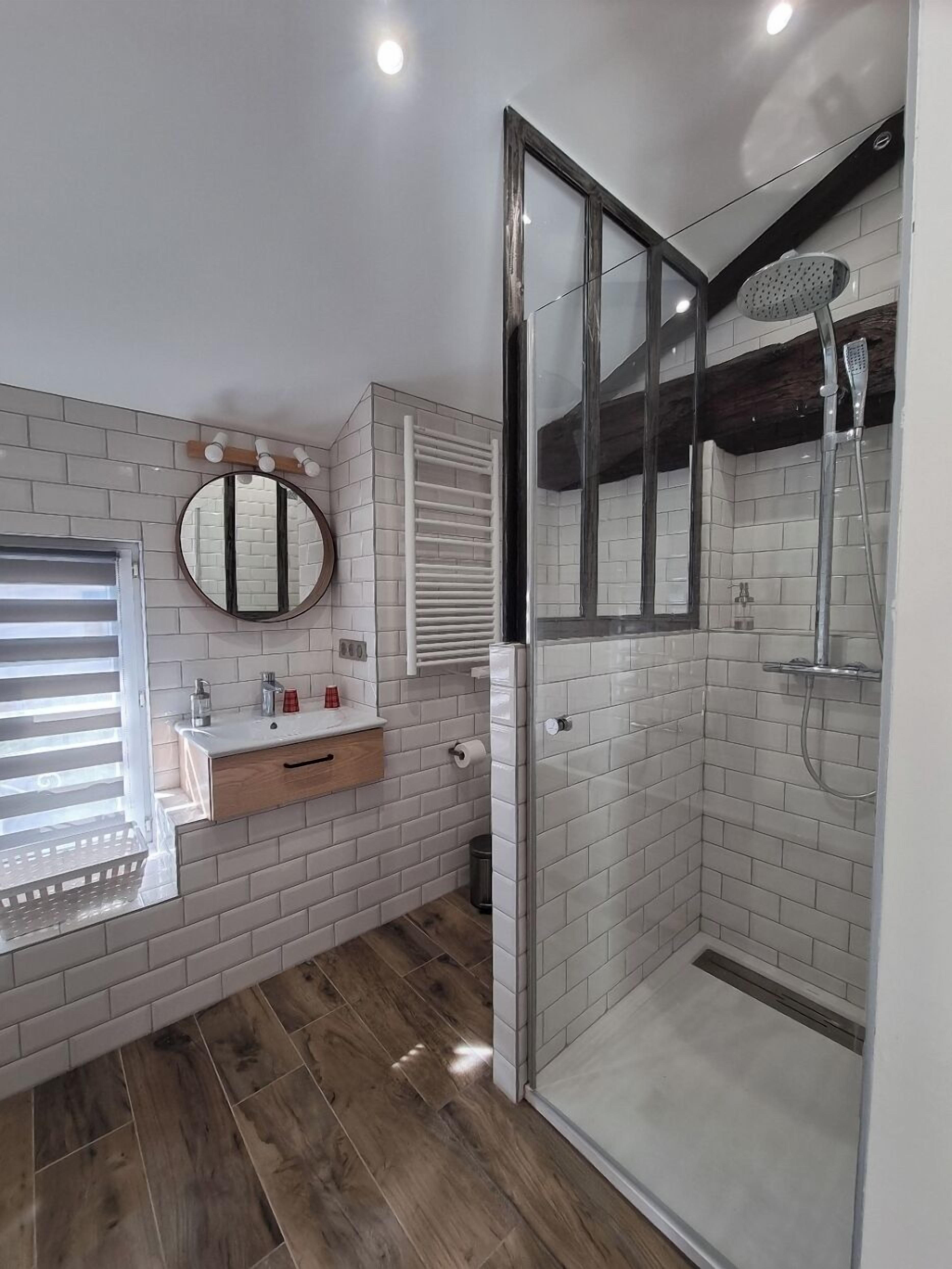 Een moderne badkamer met een glazen douchecabine, witte metrotegels, een houten wastafelmeubel en een grote spiegel.