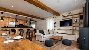 A modern kitchen with wooden cabinets, a dining table set with white plates, and a living area with a sofa and ottomans. - Le Cottage du Parc (Chambéon)