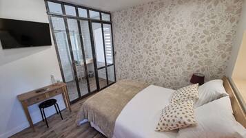 Un dormitorio con cama, escritorio, silla, televisor y ventana.