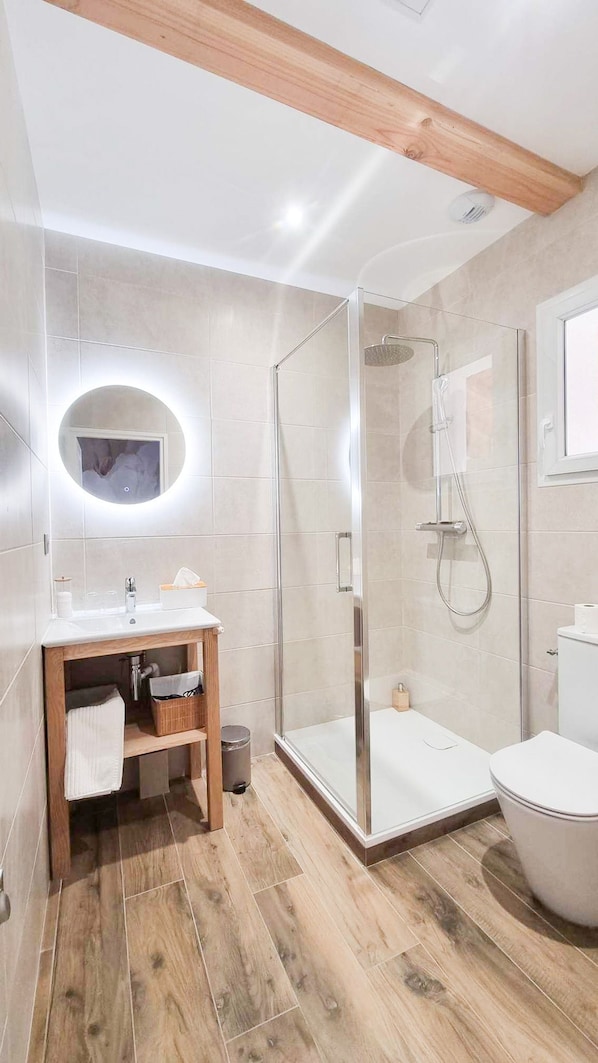 A modern bathroom with a glass-enclosed shower, a wooden vanity, and a toilet.