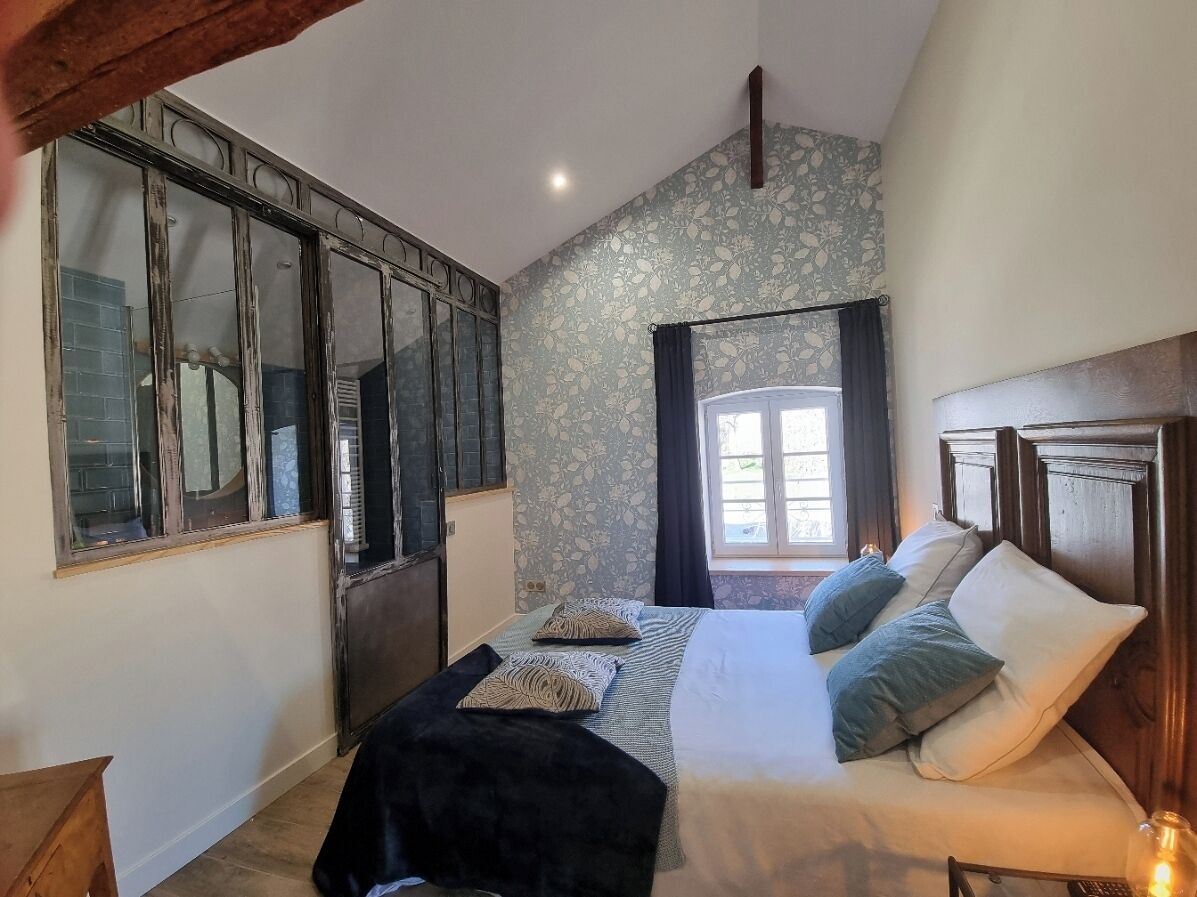 A bedroom with a large bed, a wooden headboard, a window with curtains, and a wall with a floral pattern.