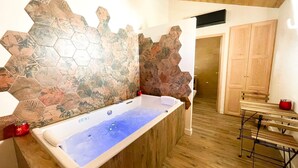 A bathroom with a bathtub, a wooden bench, and a shower area. - Le Cottage du Parc (Chambéon)