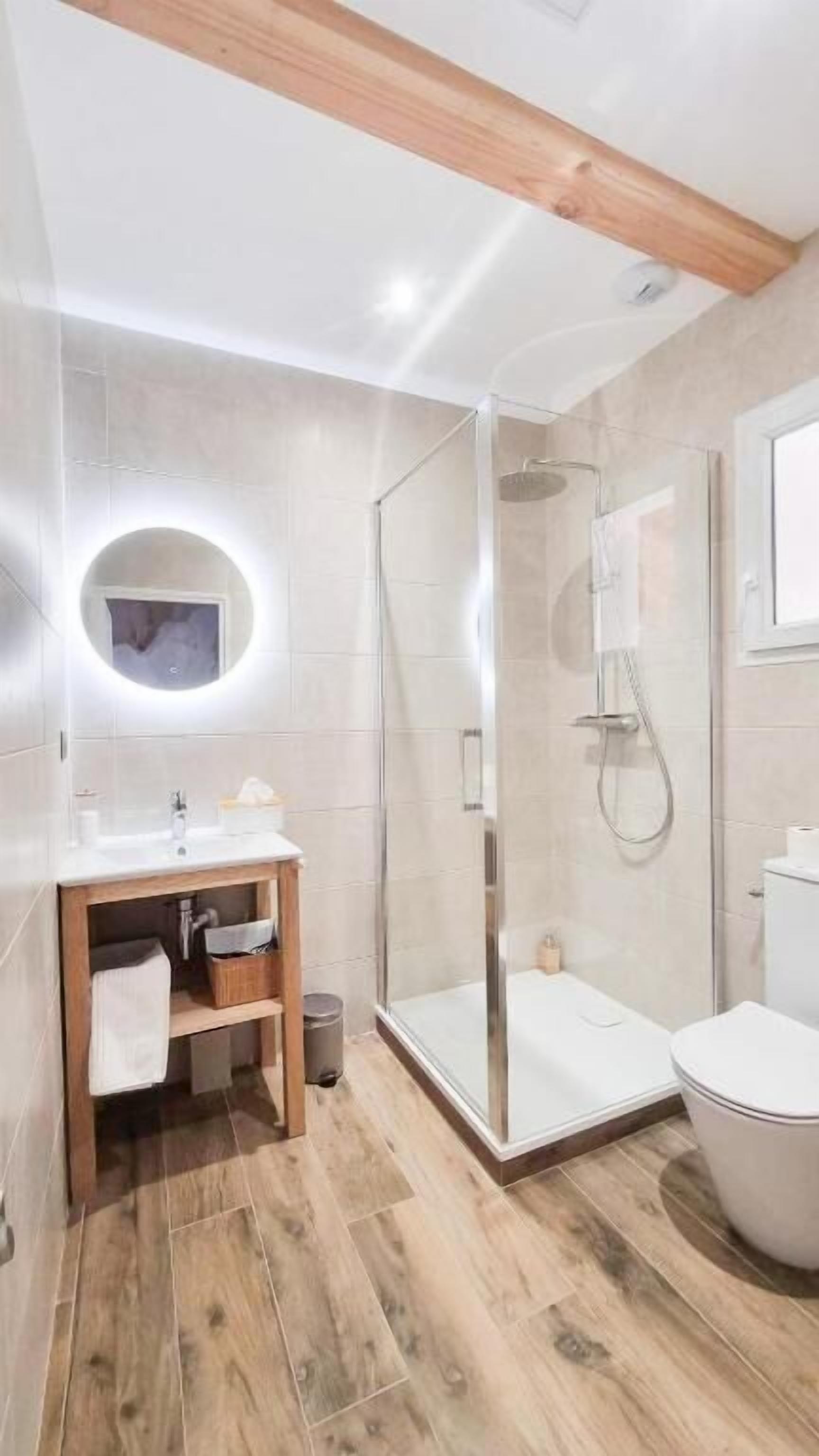 A modern bathroom with a wooden vanity, a glass shower enclosure, and a toilet.