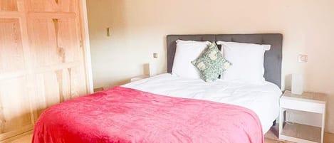 Quarto com teto de madeira, cama com manta vermelha, roupa de cama branca e mesa de cabeceira com abajur.