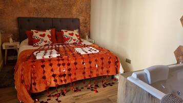 A bedroom with a large bed, a nightstand, a bedside table, and a wooden floor.