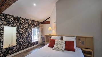 A bedroom with a large bed, a nightstand, a lamp, a window with curtains, and a wall with a floral pattern.