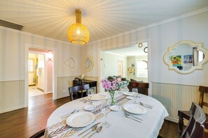 Een eetkamer met een ronde tafel gedekt voor zes personen, een kroonluchter en een spiegel met decoratieve lijst.