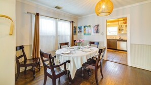 Een eetkamer met een ronde tafel voor zes personen, houten stoelen, een kroonluchter en uitzicht op de keuken.