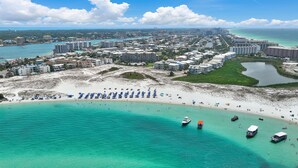 A coastal cityscape with a beach, clear turquoise waters, and a mix of residential and commercial buildings.