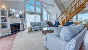 Un salon spacieux avec un haut plafond, de grandes fenêtres, une cheminée, un escalier et un coin salon confortable.