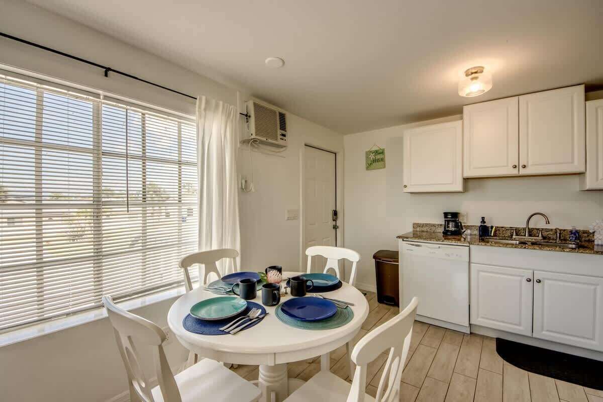 A dining area with a round table, white chairs, and a kitchen with white cabinets and a dishwasher.