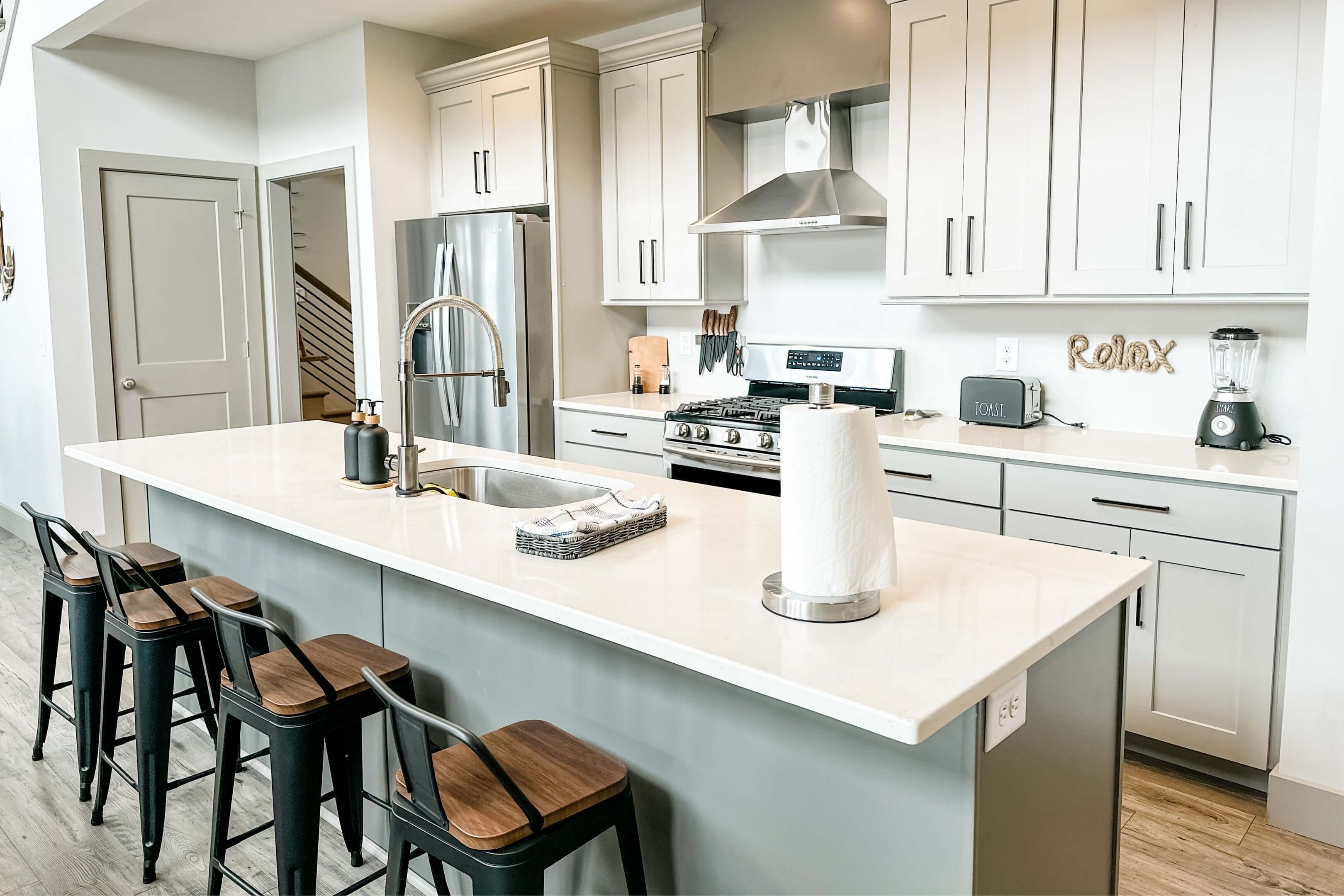 Una cocina moderna con armarios blancos, electrodomésticos de acero inoxidable y una isla central con taburetes de bar.