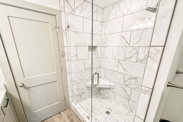 Ein modernes Badezimmer mit einer gläsernen Duschkabine, Marmorfliesen und einer weißen Tür.