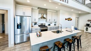 Una cocina moderna con electrodomésticos de acero inoxidable, una isla grande con taburetes de bar y una escalera que sube a un nivel superior.