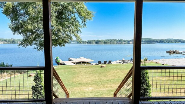 Vista desde una terraza de madera con vista a un lago, un área verde y un muelle.