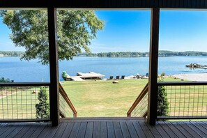 Blick von einer Holzdar Terrasse auf einen See mit einer Rasenfläche und einem Steg.