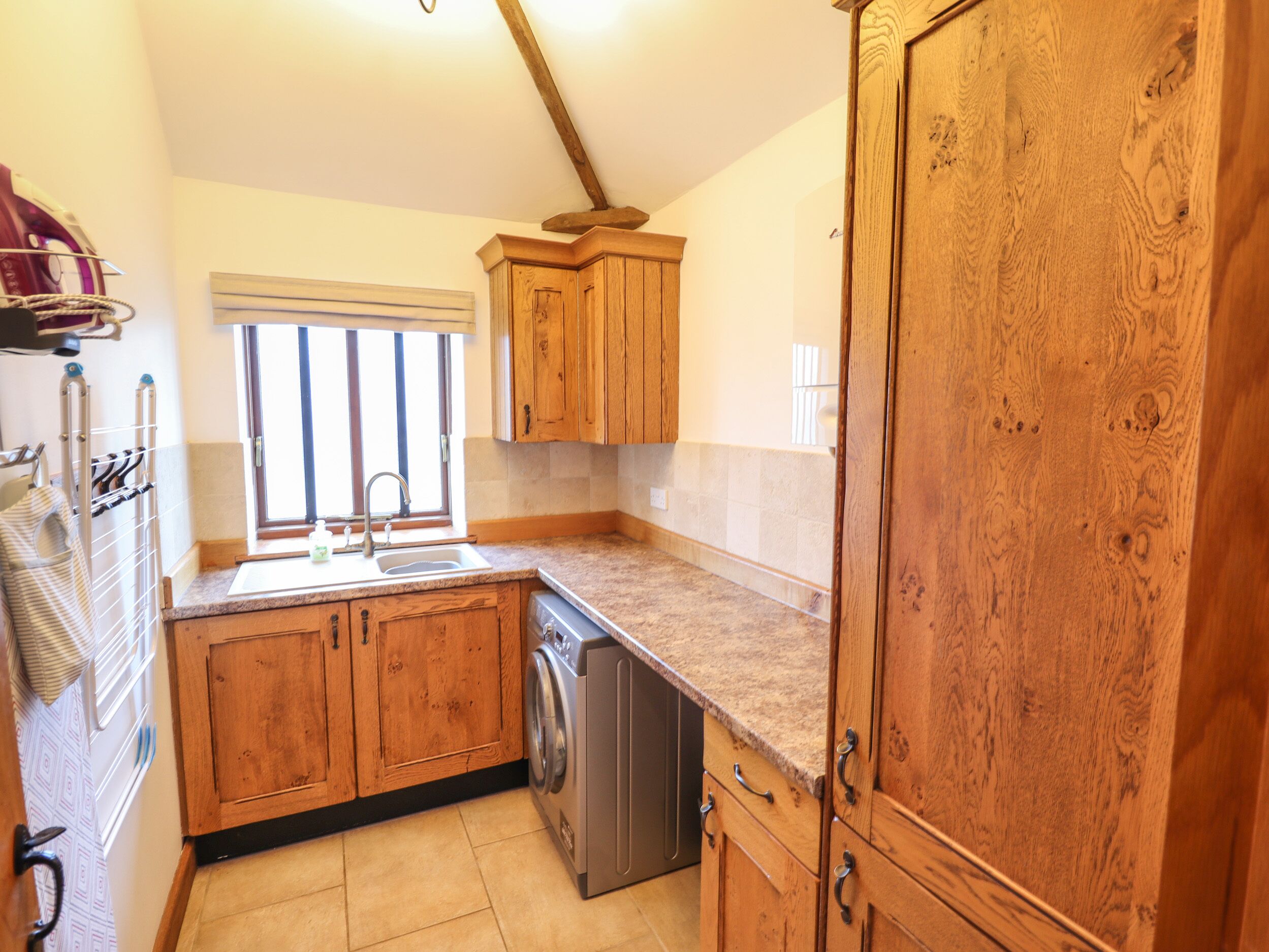 A kitchen with wooden cabinets, a stainless steel dishwasher, and a window with blinds.