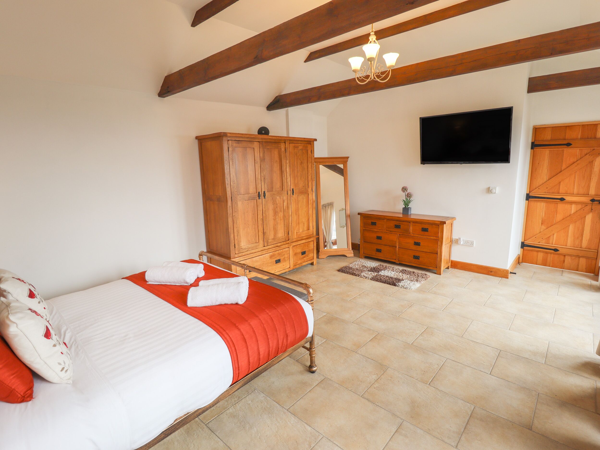 A bedroom with a bed, wooden wardrobe, a dresser, a television, and a mirror.
