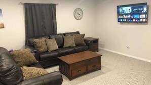 A living room with a leather sofa, a wooden coffee table, and a flat-screen TV mounted on the wall. - Garfield 4 Bedroom Close To It All! (Sioux Falls)
