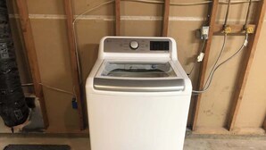 A white washing machine in a room with exposed wooden framing and a concrete floor. - Garfield 4 Bedroom Close To It All! (Sioux Falls)