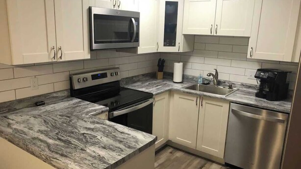 A modern kitchen with white cabinets, a stainless steel dishwasher, a microwave, and a stove. - Garfield 4 Bedroom Close To It All! (Sioux Falls)