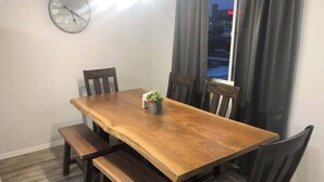 A dining area with a wooden table and benches, a clock on the wall, and a window with curtains. - Garfield 4 Bedroom Close To It All! (Sioux Falls)
