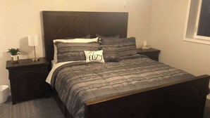 A neatly made bed with a patterned bedspread and pillows, a bedside table with a lamp, and a small plant on the nightstand. - Garfield 4 Bedroom Close To It All! (Sioux Falls)