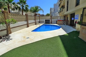 A swimming pool surrounded by a brick wall, a palm tree, and a building with a sign.