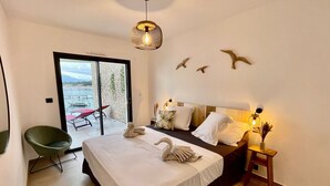 Camera d'albergo con un letto, una sedia, un tavolino, una lampada a parete e vista all'esterno.