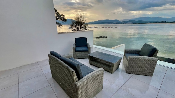 Una terrazza con mobili in vimini, ringhiera in vetro e vista sul mare e sulle montagne.