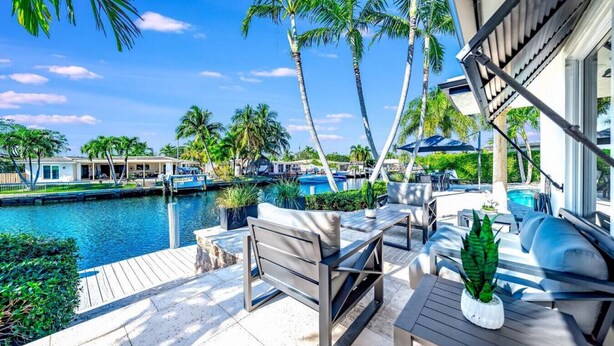 Ein Poolbereich mit Sitzgelegenheiten im Freien, Blick auf das Wasser und Palmen.